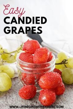 a glass jar filled with strawberries next to grapes