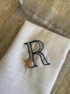 the embroidered letter r is on top of a white napkin with a gold rose in it