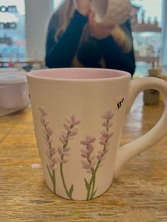 a coffee cup with pink flowers painted on the side and a woman looking at it