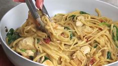 someone is using tongs to stir noodles in a white bowl with chicken and spinach