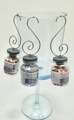 three jars are sitting on top of a glass stand, with metal wire and beads in them