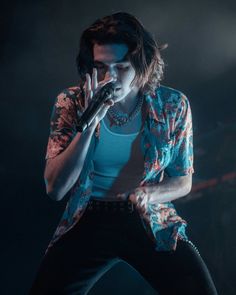 a male in a blue shirt and black pants holding a microphone to his ear while standing on stage