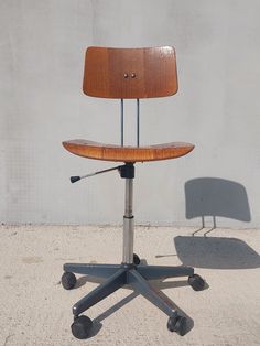 an office chair sitting on top of a metal base with wheels in front of a concrete wall