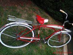 a red and white bicycle parked on the grass next to a curb with trees in the background