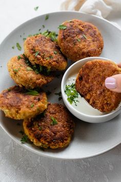 a person dipping something into a small bowl on top of a plate with crab cakes