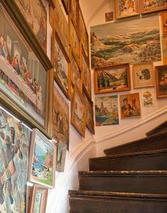 many framed pictures hang on the wall next to a stair case filled with paintings and artwork