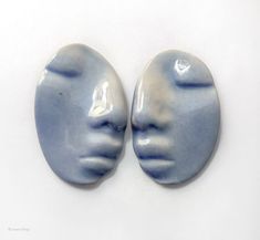 two ceramic faces are shown on a white surface, one is blue and the other is gray