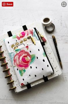 an open notebook with flowers on it next to a cup of coffee and some scissors