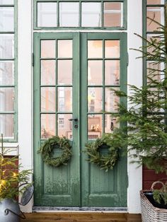 two wreaths are on the front door of a house with green doors and windows