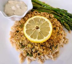 a plate with asparagus, lemon and rice on it next to a bowl of sauce