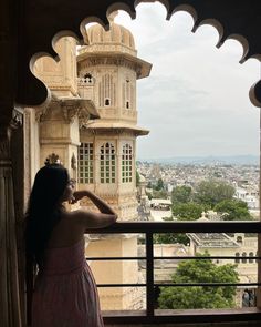 a woman in a pink dress standing on a balcony looking out at the city below