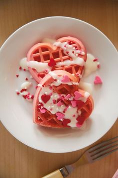 two heart shaped waffles on a plate with white icing and sprinkles