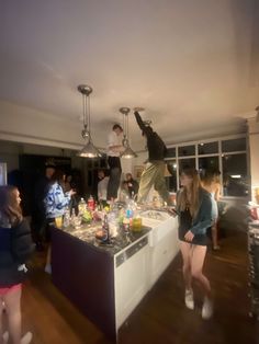 a group of people standing around a kitchen island with drinks on it and one person jumping in the air