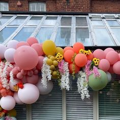 a bunch of balloons hanging from the side of a building with flowers and daisies on them