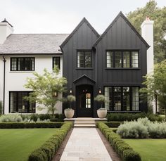 a large black and white house with lots of plants in the front yard, surrounded by greenery