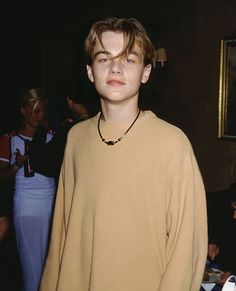 a young man standing in front of a mirror wearing a tan sweater and beaded necklace