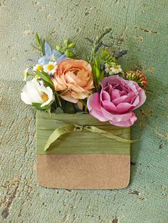 an arrangement of flowers is placed on the ground in a small green box with a ribbon