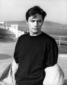 a black and white photo of a young man with gloves on his hands, standing in front of the ocean