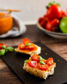 two pieces of bread with tomatoes and basil on top sitting on a black plate next to bowls of vegetables