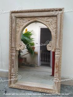 a large mirror sitting on top of a floor next to a potted palm tree