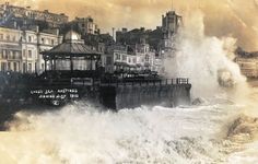 an old photo of waves crashing into the shore in front of some buildings and water