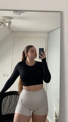 a woman taking a selfie in front of a mirror wearing high waist shorts and black crop top