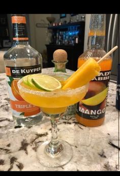 a glass filled with an orange and lime drink next to two bottles of alcohol on a marble counter top