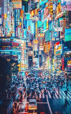 many people with umbrellas are crossing the street in front of tall buildings at night