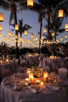 an outdoor dining area with many tables and chairs covered in white linens, lit by lanterns