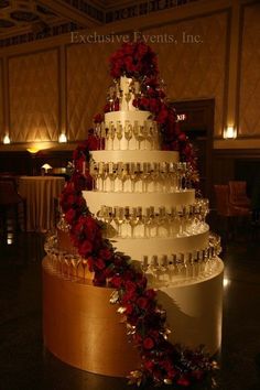 a wedding cake with wine glasses and roses on the bottom tier is decorated in gold