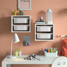 a white desk topped with two bins filled with crafting supplies next to a pink wall