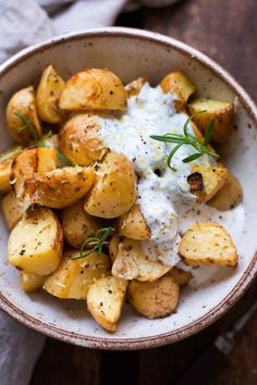 a white bowl filled with potatoes covered in sour cream and garnished with fresh herbs