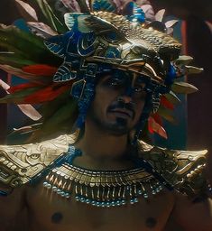 a man in an elaborate headdress with feathers on his face and chest, standing next to a mirror