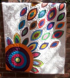 a quilted wall hanging on the side of a brick building with colorful circles and leaves