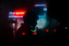 the silhouette of a man talking on his cell phone in front of a city street at night