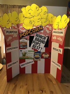 a pop corn display on a wooden table with paper cut outs and yellow balloons above it