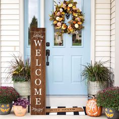 a welcome sign sitting in front of a door with potted plants and pumpkins