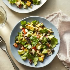 two plates with salad on them next to a glass of water and silver spoons