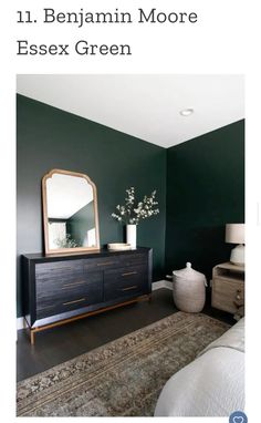 a bedroom with dark green walls and white bedding, an area rug and a large mirror