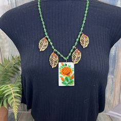 a woman wearing a black top and green beaded necklace with orange flowers on it