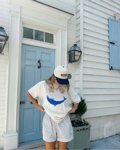 a woman standing in front of a blue door wearing a white shirt and striped shorts