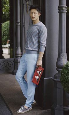 a young man standing on the sidewalk holding a red purse and posing for a photo