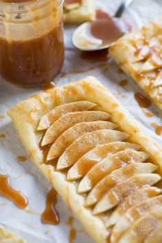 caramel apple pies are sitting on wax paper and next to jars of caramel sauce