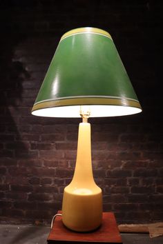 a green lamp sitting on top of a wooden table next to a brick wall in a room