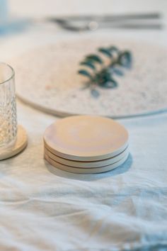 two plates and a glass on top of a white table cloth with pine cones in the background