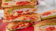 four sandwiches stacked on top of each other with tomatoes and pesto in the middle