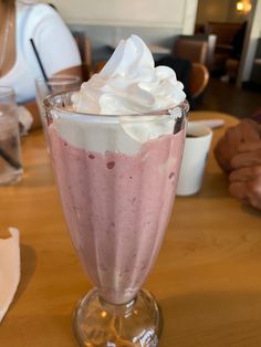 a dessert in a glass with whipped cream on top sits on a table at a restaurant