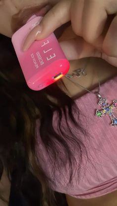 a woman in pink shirt holding up a bottle with cross charms on it and an earring