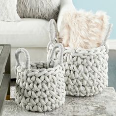 two woven baskets sitting on top of a rug in front of a white couch and coffee table