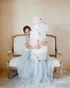 a woman sitting on a chair holding a stack of suitcases